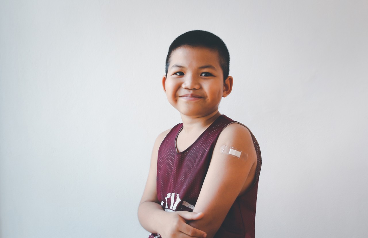 Asian boy with showing his arm for vaccine injection smiling with a happy after getting covid-19 vaccine.