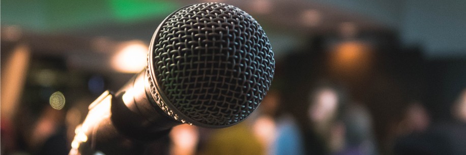 A close-up of a microphone in a microphone stand with blurry background including people outside at an event.