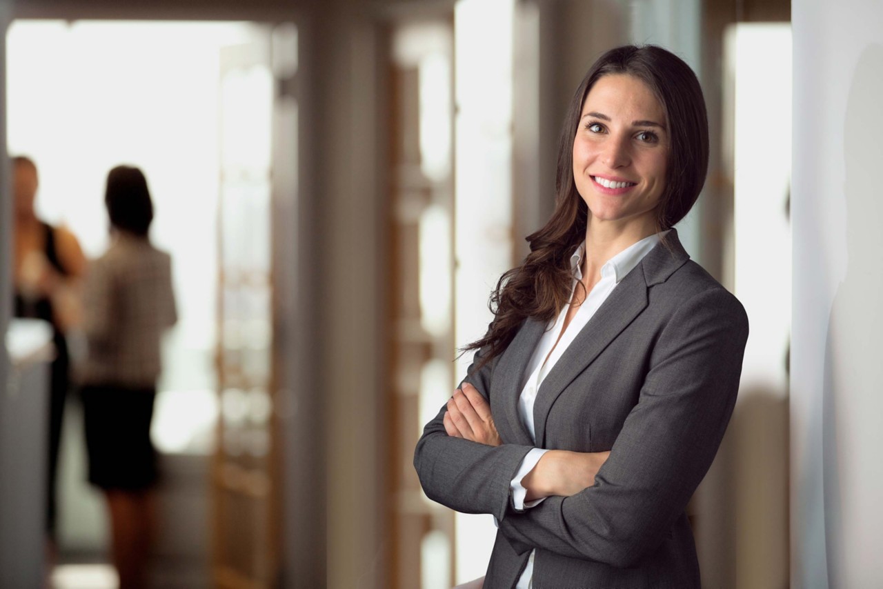 Woman smiling and standing in a hallway or open room.