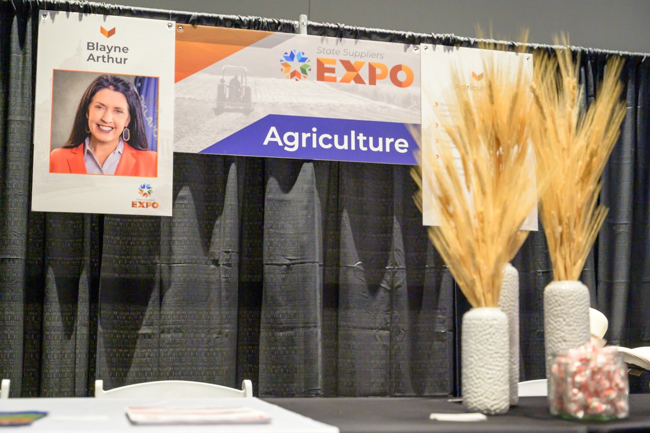 Agriculture cabinet booth behind three vases of wheat.