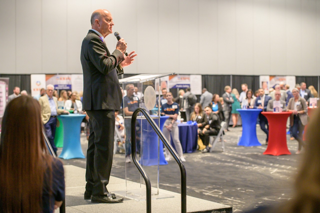 State Chief Operating Officer John Suter speaking on the ballroom stage.