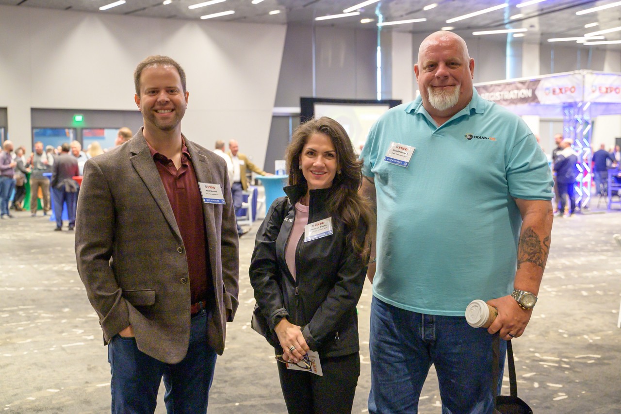 Three attendees stand and smile in the ballroom.