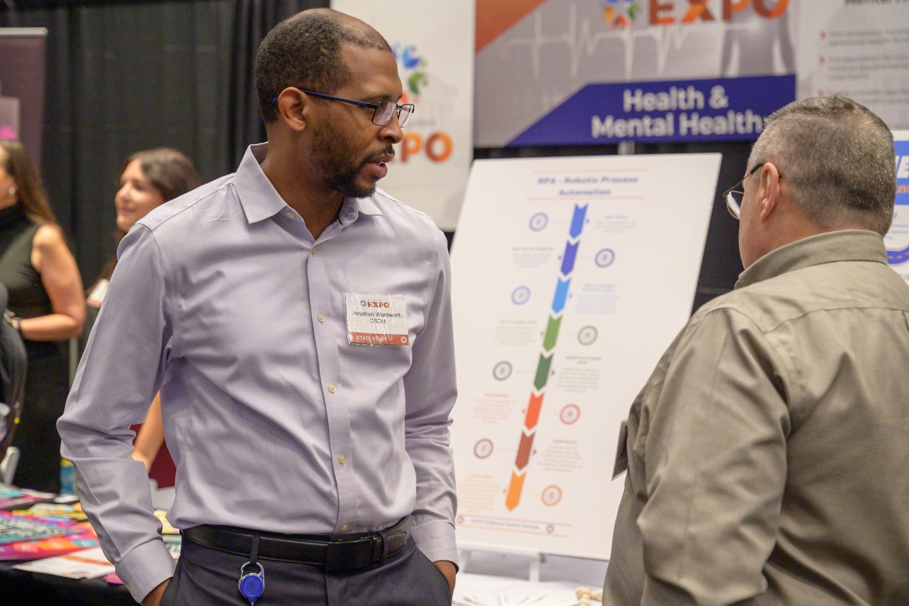 Two people chat in front of Health and Mental Health cabinet booth.