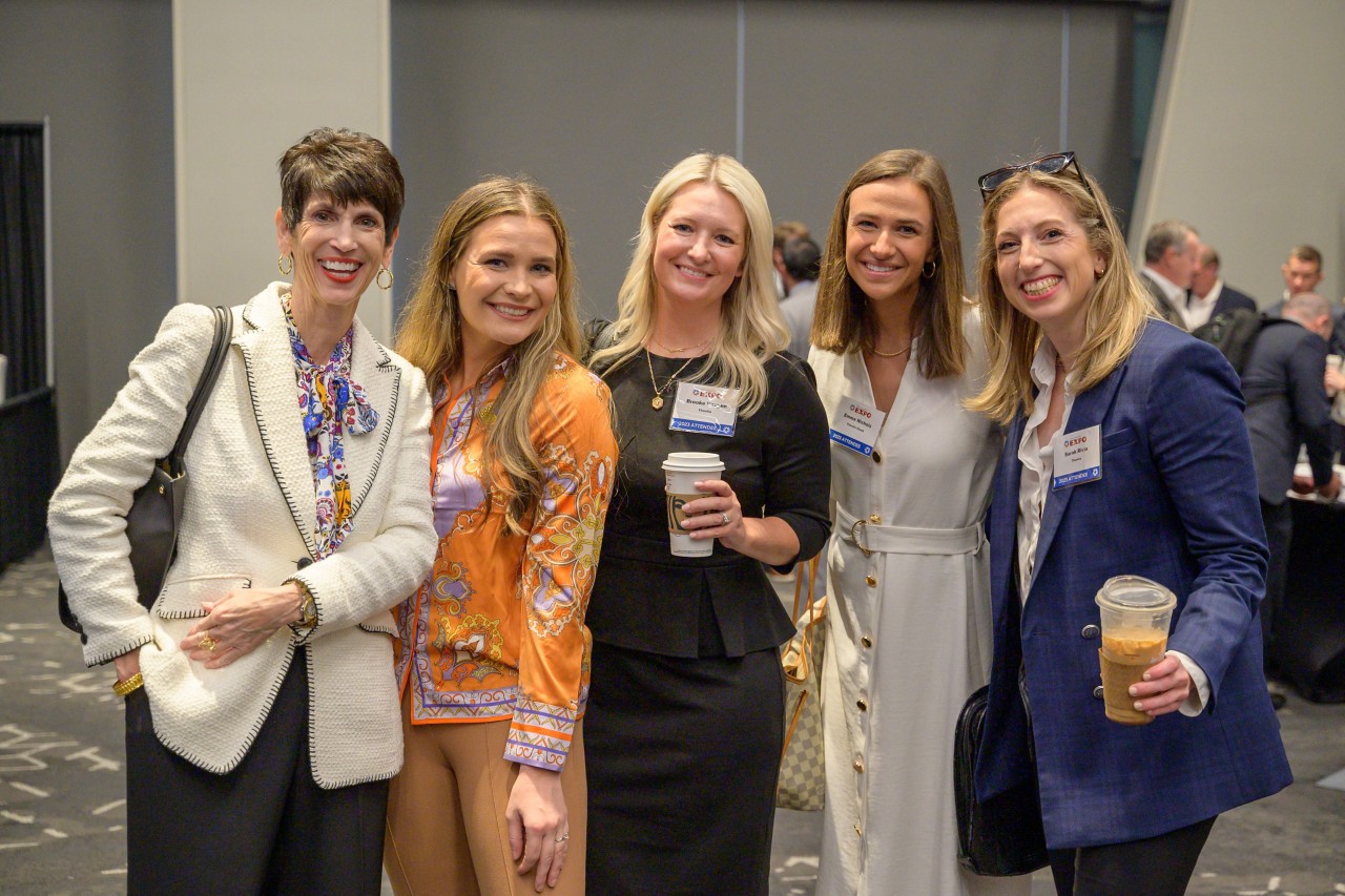 Yasmine Barve and Bonnie Campo smile and pose with three attendees from Thentia in the ballroom.