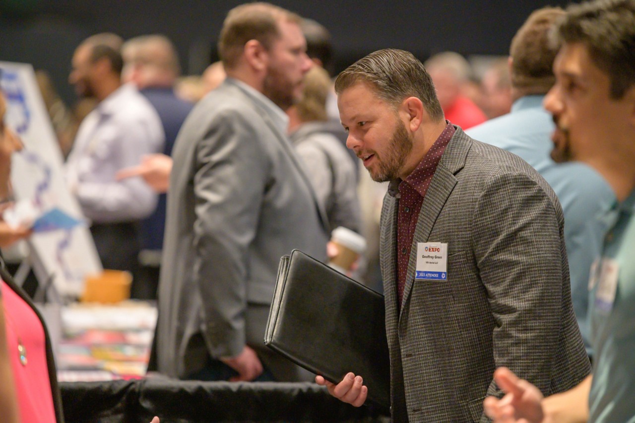 Attendee from VSI Aerial LLC talking at ballroom bistro table.